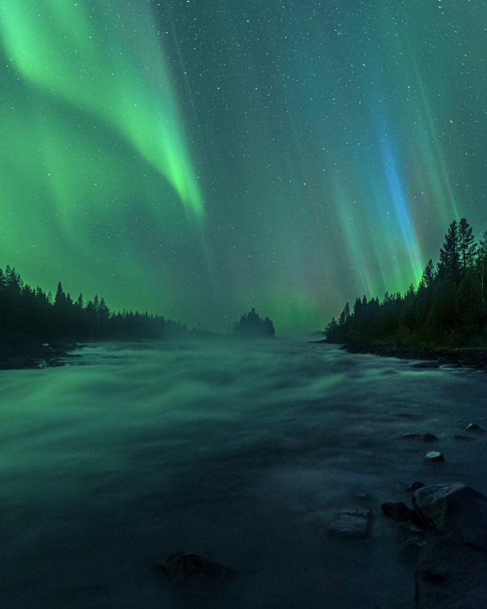 Un fiume sotto un cielo verde e blu pieno di luci aurore