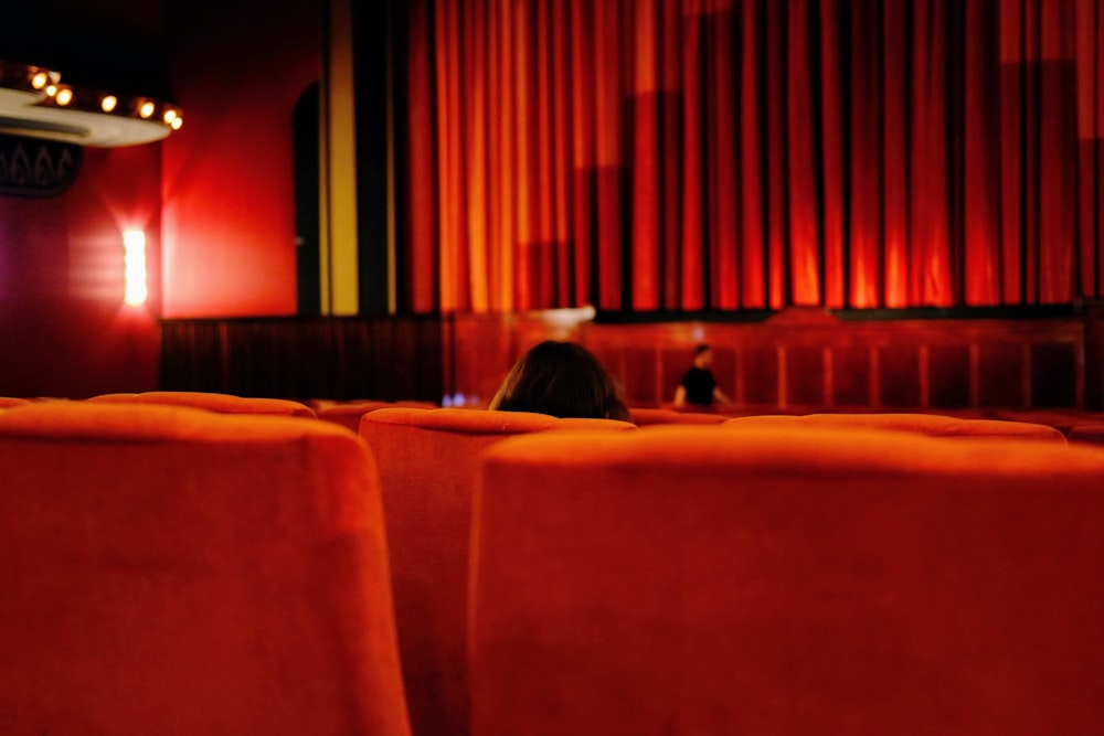 a person sitting in a red chair in front of a red curtain