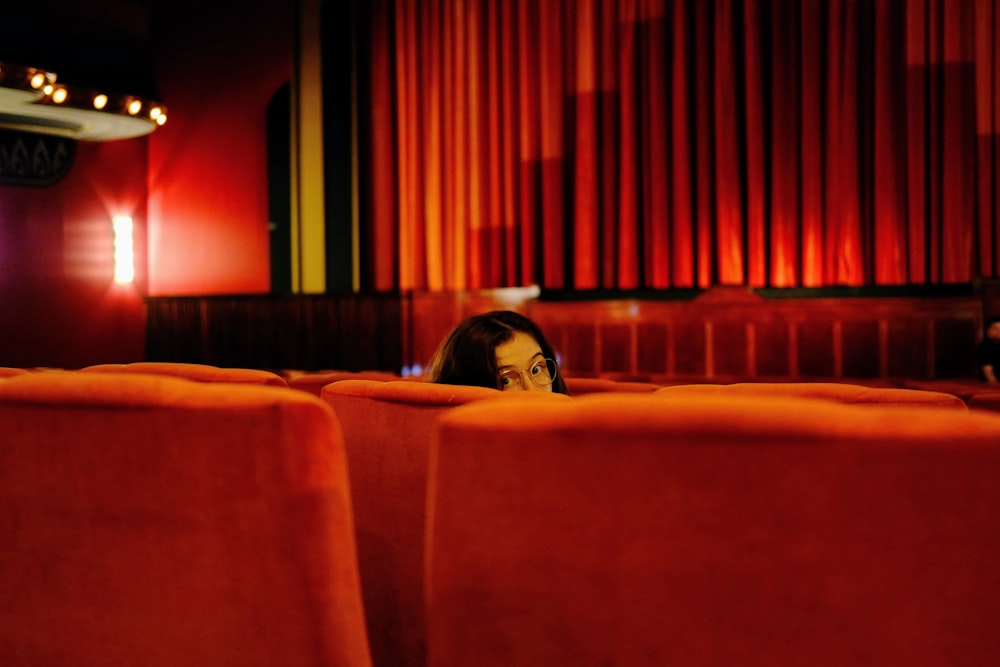 a woman sitting in a red chair in front of a red curtain