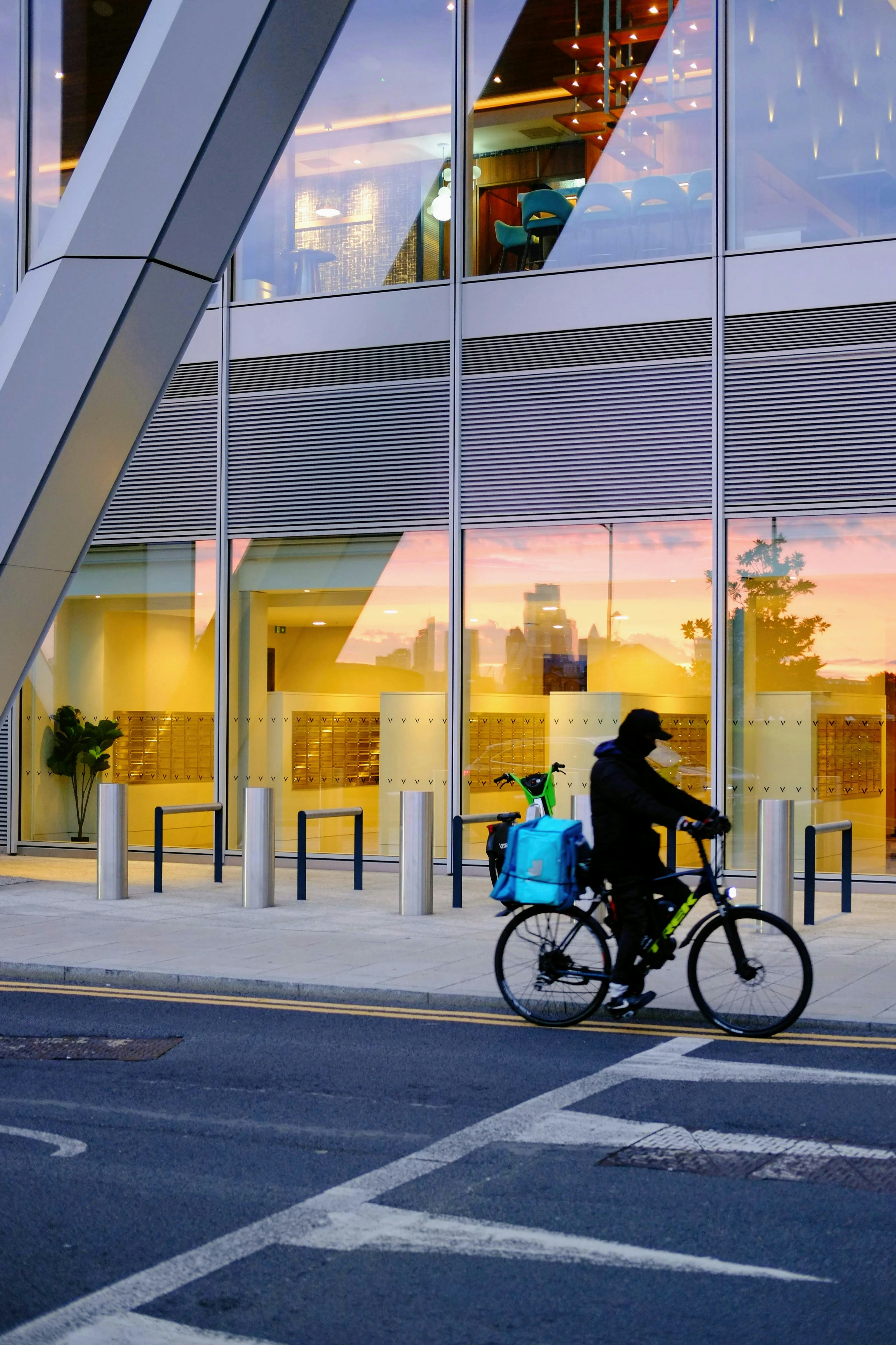 Cyklist leverer pakker forbi en moderne bygning ved solnedgang.