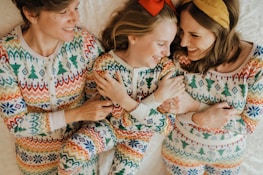 Three people are lying down on a white surface, all dressed in matching colorful patterned pajamas. They appear to be smiling and interacting warmly with each other.