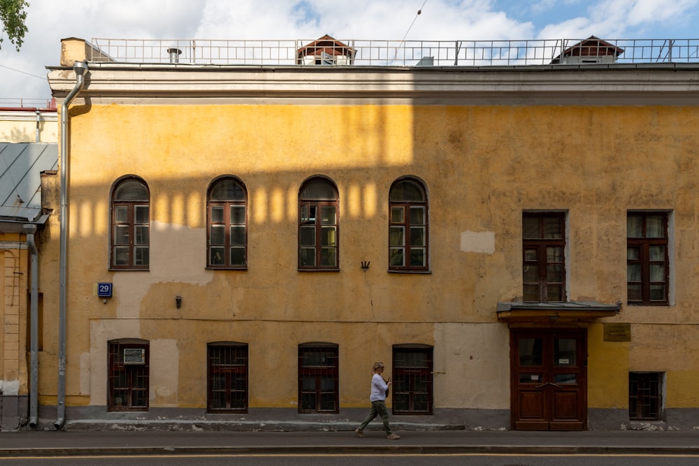 a man walking down a street past a tall yellow building