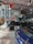 An indoor setting of a vintage garage featuring classic cars and retro signs. Prominent is a large red and blue Pontiac sign with other advertisements like Avon Tyres and Champion on the wall. Displayed are a black vintage car with whitewall tires and a modern blue Porsche, contributing to an interesting blend of old and new automotive aesthetics.