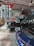 An indoor setting of a vintage garage featuring classic cars and retro signs. Prominent is a large red and blue Pontiac sign with other advertisements like Avon Tyres and Champion on the wall. Displayed are a black vintage car with whitewall tires and a modern blue Porsche, contributing to an interesting blend of old and new automotive aesthetics.