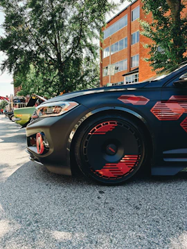 Close-up of a sleek black car with a bold red lip and custom wheels parked on asphalt.