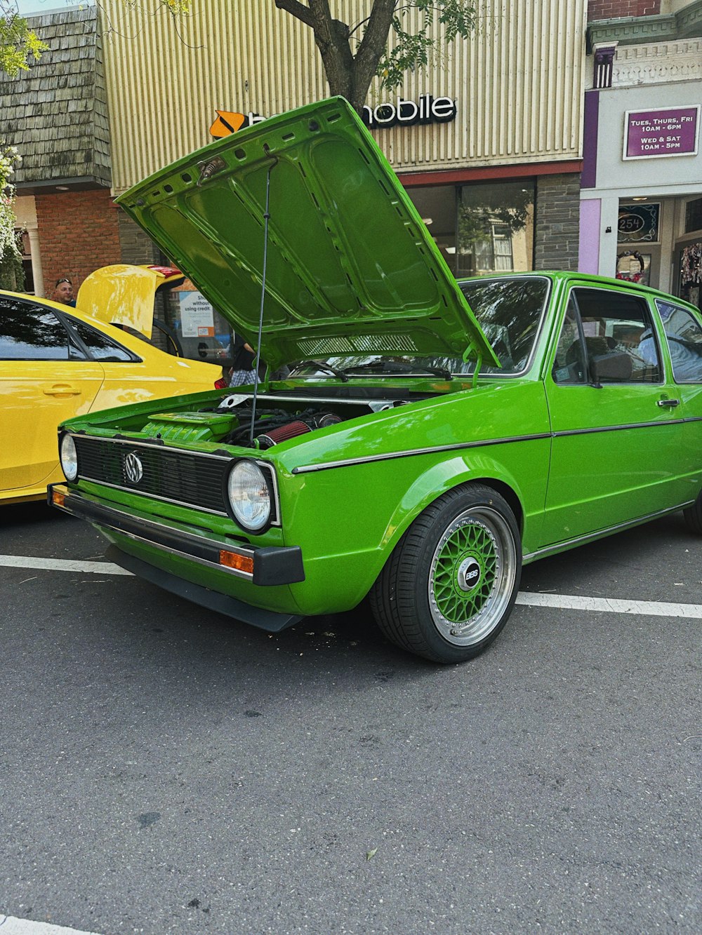 a green car with its hood open in a parking lot