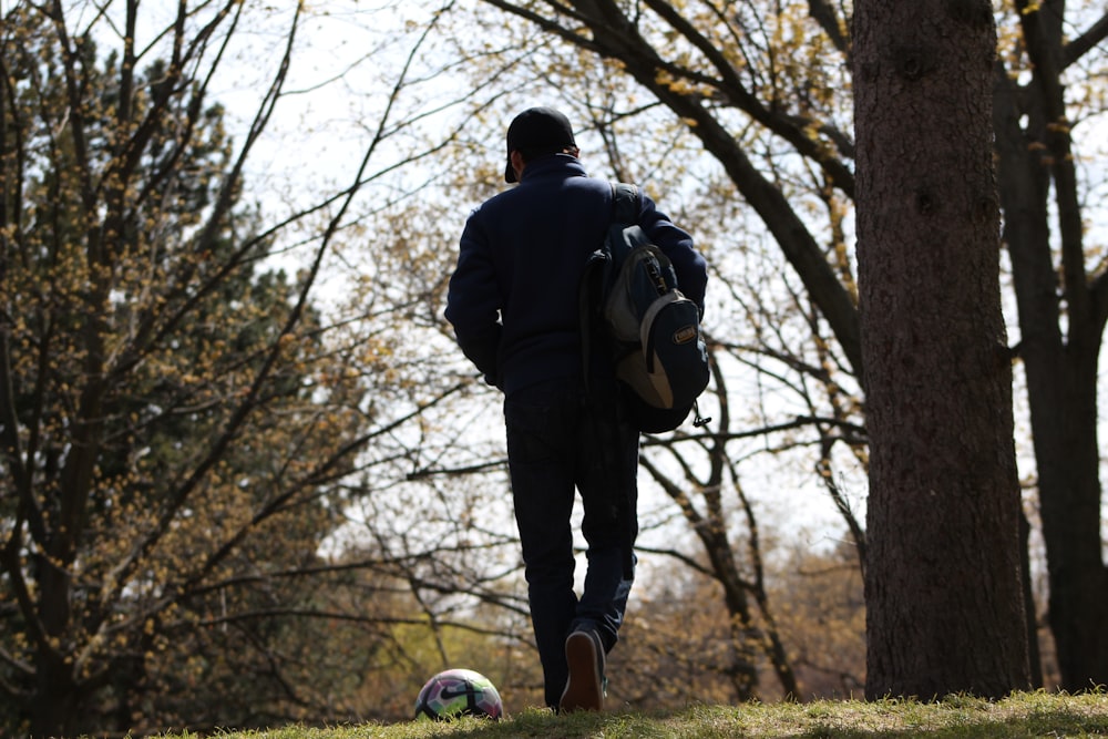 a man with a back pack walking towards a soccer ball