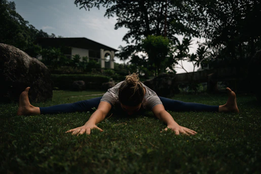 A person stretching outdoors in the morning sunlight, surrounded by greenery.