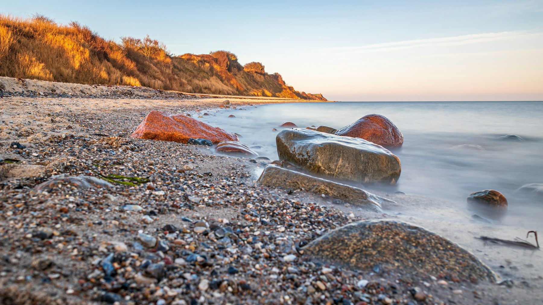 Sweeping coastal Connecticut shoreline at golden hour, calm blue water, dramatic amber sky