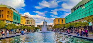 A wide-angle view of a sparkling urban fountain with people enjoying the refreshing atmosphere.