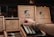 A hand reaches into a box of cigars with artistic branding on a shelf. The box features a prominent profile of a man's silhouette alongside the logo and text, indicating the brand's focus on craftsmanship. The wooden display boxes are intricately designed, showcasing premium cigars.