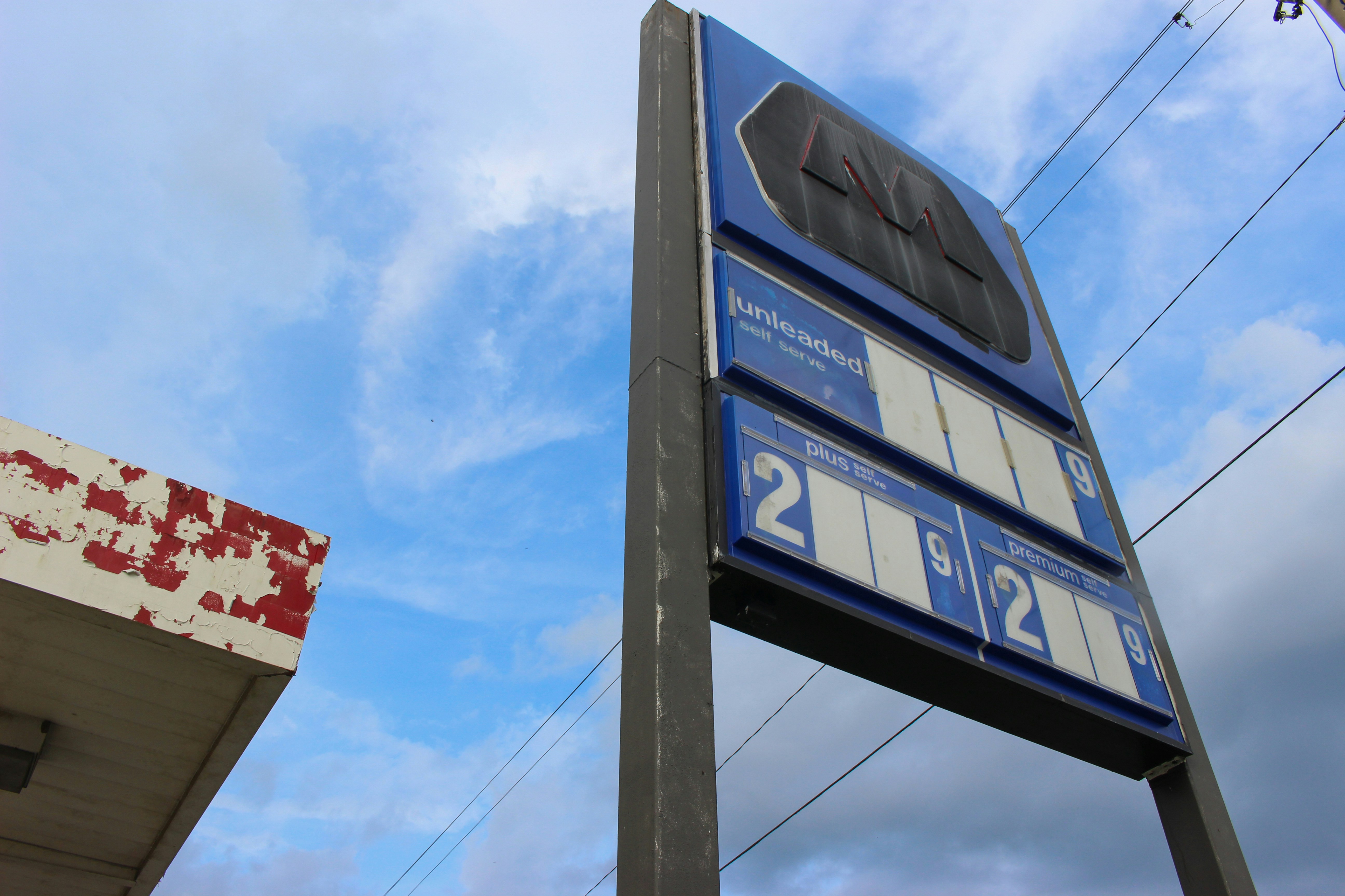 Cars refueling at a gas station with fuel price board showing gasoline prices