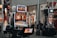 A collection of slot machines is situated inside a building with bright, colorful screens displaying various games and gaming themes. A person is seated nearby, seemingly relaxed with luggage beside them, and the atmosphere is lively with electronic displays.