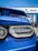 A close-up view of the rear of a blue car, focusing on its taillight and spoiler. The background shows an automotive dealership with logos for Chevrolet, Buick, and GMC, indicating a car sales setting.