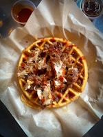 Close-up of a crispy fried chicken piece resting on a fluffy waffle with syrup dripping.