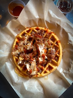 A close-up shot of crispy golden fried chicken atop fluffy, buttery waffles drizzled with maple syrup.