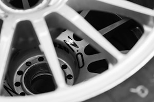 Close-up view of a wheel rim, showing the spokes and central hub. The image is in black and white, highlighting the metallic texture and details of the wheel, including the presence of certain markings or numbers on the hub.