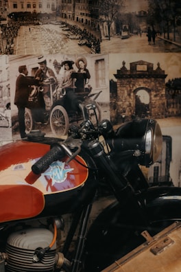 A vintage motorcycle with a prominent MV logo parked against a backdrop of sepia-toned historical photos. The images include scenes of people in early 20th-century clothing and architecture, evoking a sense of nostalgia.