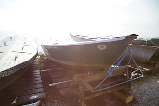 Several boats are positioned on a wooden dock, partially covered with tarps and secured with ropes. The sunlight is creating a strong glare, making parts of the image overexposed. The dock is made of wood planks, and the boats appear to be inactive, possibly stored for off-season.