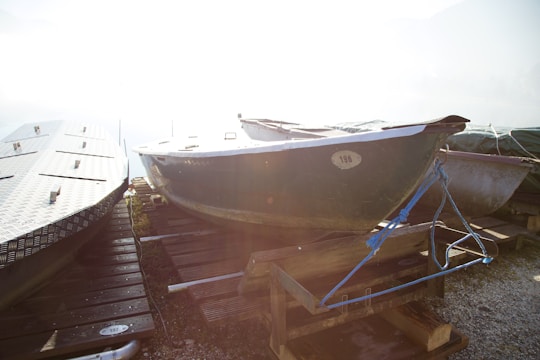 Several boats are positioned on a wooden dock, partially covered with tarps and secured with ropes. The sunlight is creating a strong glare, making parts of the image overexposed. The dock is made of wood planks, and the boats appear to be inactive, possibly stored for off-season.