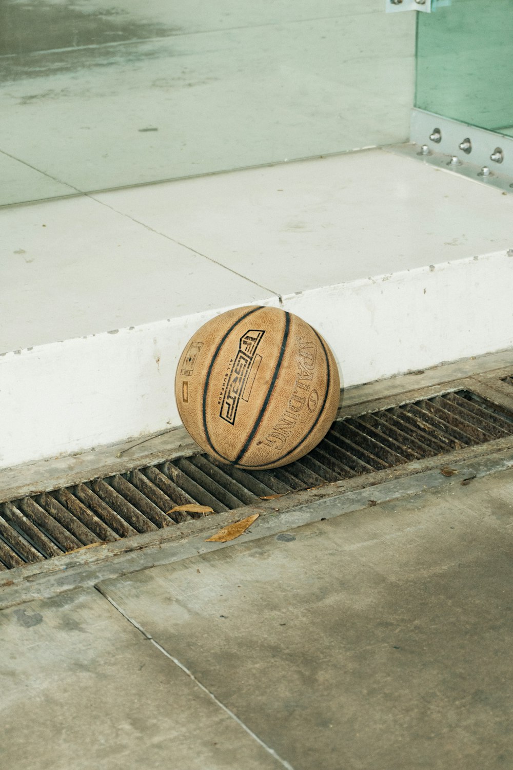 Una pelota de baloncesto sentada en el suelo junto a una rejilla de drenaje