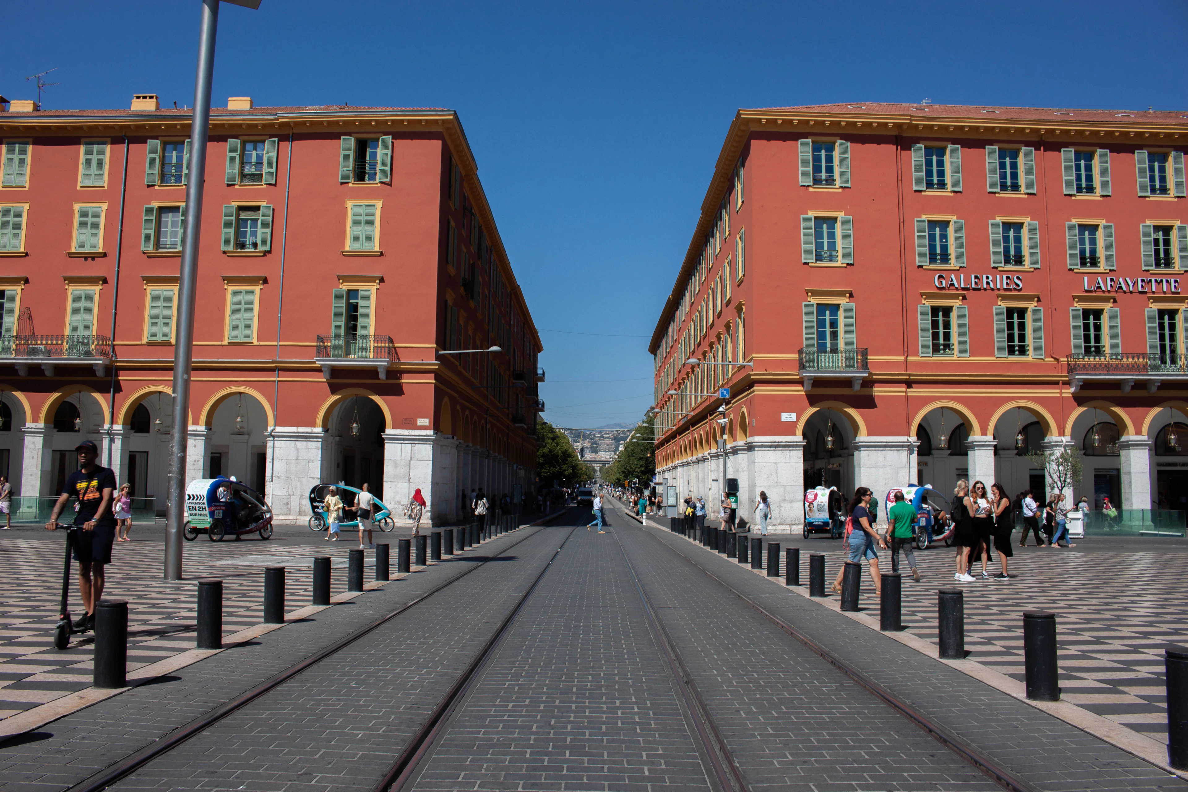 Place Masséna's red arcaded buildings and checkered pavement in Nice on a sunny day.