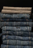 Stack of neatly folded pants in earthy tones on a rustic shelf.