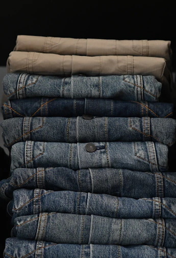 A neatly folded stack of colorful, casual trousers on a wooden table.