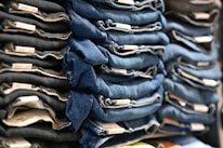 Neatly folded stacks of blue and black denim jeans are organized on display, showcasing tags on the folded edges.