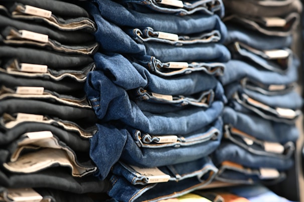 Neatly folded stacks of blue and black denim jeans are organized on display, showcasing tags on the folded edges.