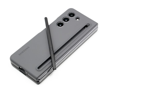 A sleek, gray Samsung smartphone is placed on a white surface with a stylus resting diagonally across it. The phone's design includes a visible camera module with multiple lenses.