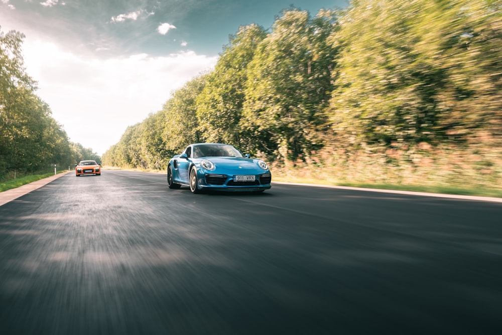 a blue sports car driving down a road next to a forest