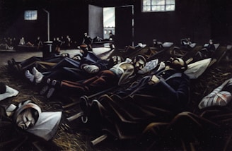 A dimly lit room filled with several people lying on the floor, appearing to be resting or injured. The scene has a somber atmosphere with light streaming in through a window and an open door, illuminating parts of the room.