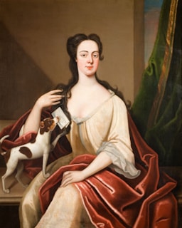 A model in elegant fashion attire gently holding a calm, regal-looking dog.