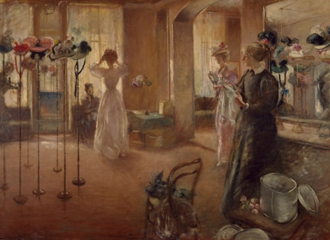 A softly lit room filled with elegant hats displayed on tall stands. Three women are present, with one adjusting a hat in front of a mirror. Another woman holds a hat while standing, and a third sits quietly. The atmosphere is calm and genteel, reminiscent of a past era. The walls and floor have a warm, brown hue, complementing the delicate fabric of the hats.
