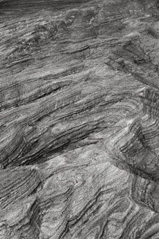 A close-up view of textured rock surface with layered patterns and striations creating an intricate design. The surface appears rugged and natural, showcasing geological formations and natural rock patterns.