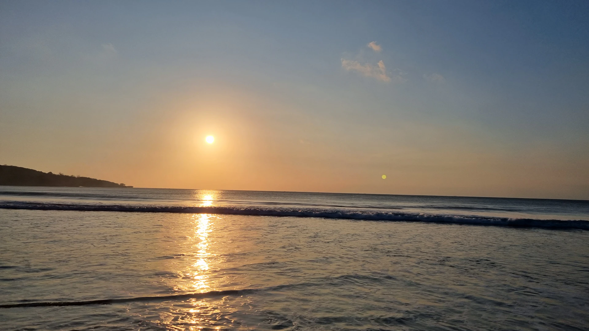 A high-resolution photo capturing a serene sunset over a calm sea, highlighting warm golden tones and soft reflections.