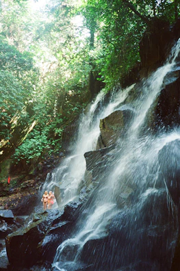 A couple exploring a hidden waterfall in a lush tropical forest.