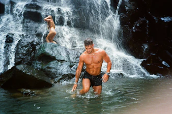 a man standing in a body of water next to a waterfall