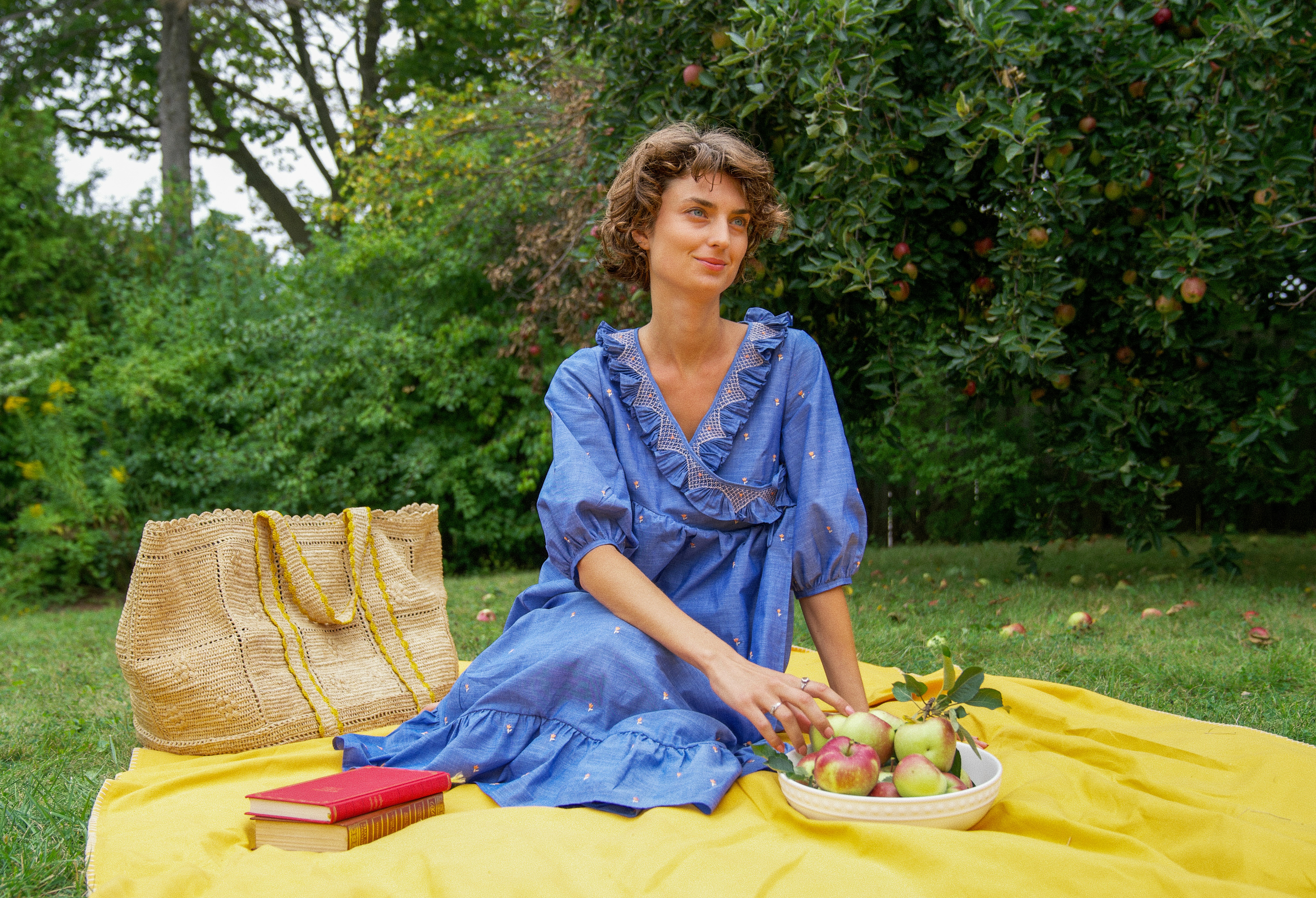 a woman sitting on a blanket with a basket of fruit