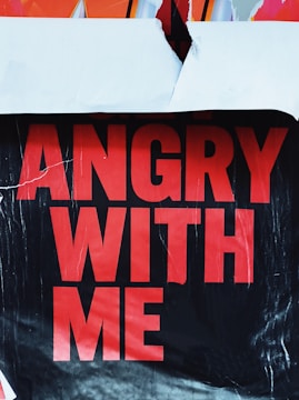 A partially torn poster with bold red text that reads 'ANGRY WITH ME' on a black background.