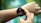 A smartwatch on a person's wrist displays heart rate information and a warning about potential heart attack detection. The watch has a black strap and the display shows a heart rate of 112 bpm with red waveform graphics. Another hand is pointing to or interacting with the watch.