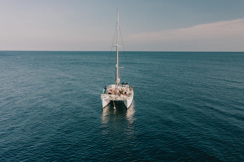 Group of friends laughing and relaxing on the deck of a catamaran, surrounded by calm ocean waves.