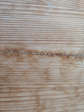 Close-up of a craftsman carefully filling a wooden floor crack with matching wood filler.