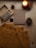 A wooden surface is adorned with a cozy, mustard-colored sweater, an open box of alphabet stamps, a burning candle in a small jar, a notebook with 'AUTUMN' embossed on its cover, and two pinecones. The items are arranged in an aesthetically pleasing manner, evoking a sense of warmth and comfort.