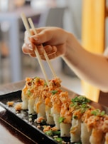 A hand holding chopsticks picking up a piece of nigiri sushi over a black plate.