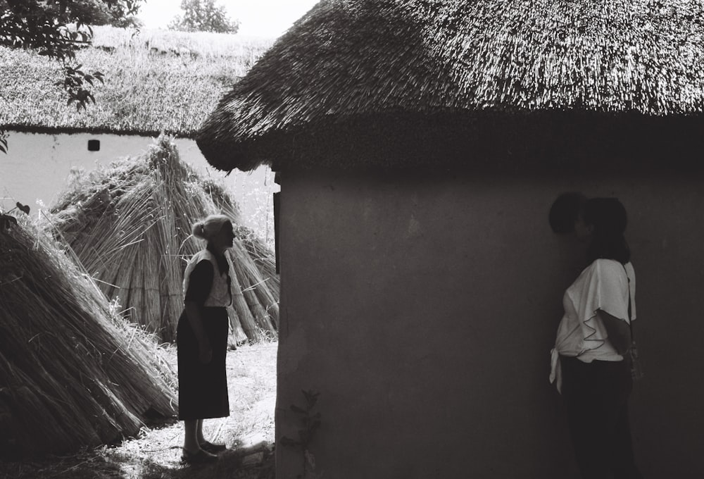 a woman standing next to a hut next to a man