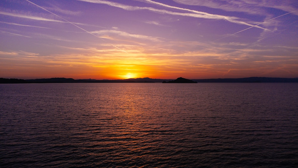 a sunset over a body of water with contrails in the sky