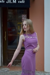 a woman in a purple dress standing in front of a cafe