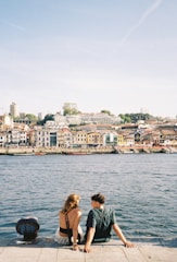 a man and a woman sitting on a dock next to a body of water